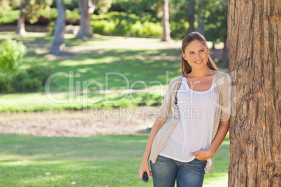 Woman with a cellphone leaning against a tree