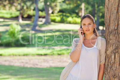 Woman on the cellphone leaning against a tree