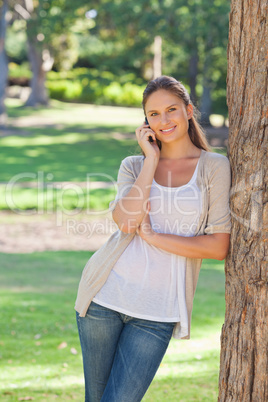 Smiling woman on her cellphone leaning against a tree