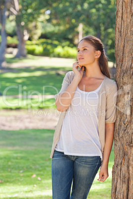 Woman talking on the phone while leaning against a tree