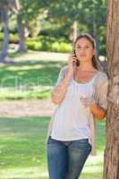 Woman talking on her phone while leaning against a tree
