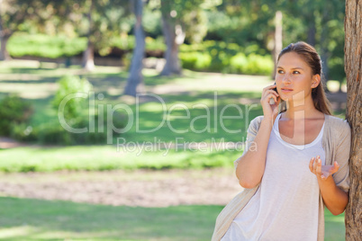 Woman talking on her cellphone while leaning against a tree