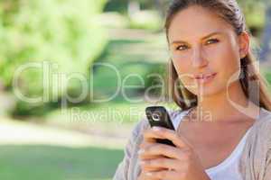 Close up of woman holding her mobile phone in the park