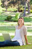 Smiling woman with her laptop sitting in the park