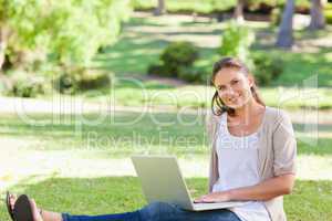 Smiling woman sitting on the grass with her laptop