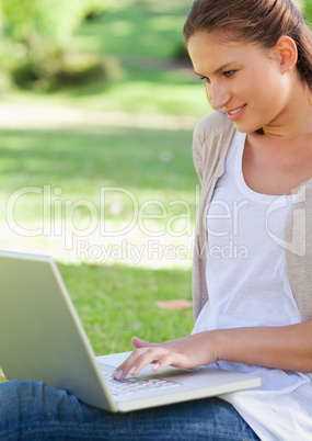 Smiling woman using her laptop while sitting on the lawn