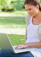 Smiling woman using her laptop while sitting on the lawn