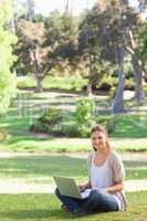 Smiling woman sitting on the lawn with her laptop