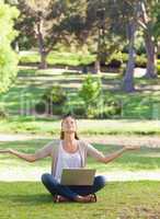 Woman sitting on the lawn in a yoga position with a laptop
