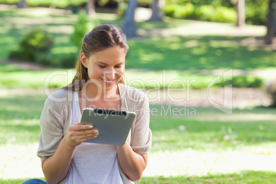 Smiling woman with her tablet computer sitting on the lawn