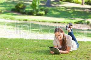 Smiling woman lying on the lawn with a tablet computer