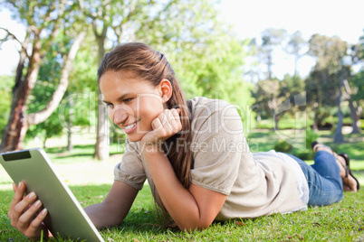 Smiling woman laying on the lawn with her tablet computer