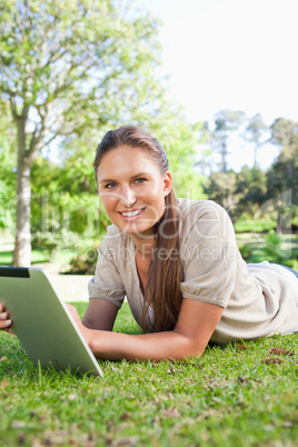 Smiling woman lying on the grass with her tablet computer