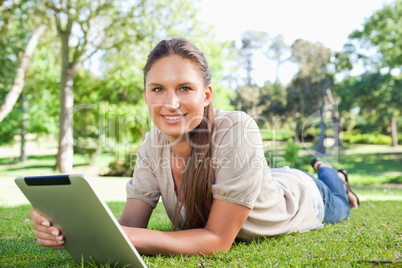 Smiling woman with her tablet computer lying on the lawn