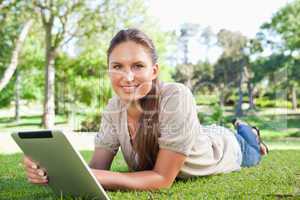 Smiling woman with her tablet computer lying on the lawn