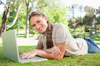 Smiling woman lying on the lawn with her laptop