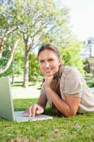 Smiling woman with her laptop while lying on the lawn