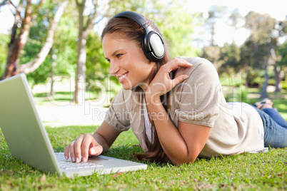 Woman with a laptop and a headset lying on the lawn