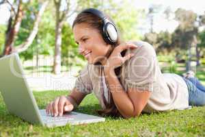 Woman with a laptop and a headset lying on the lawn