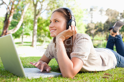 Smiling woman with headphones and a laptop lying on the lawn