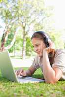 Woman with headphones and a laptop lying on the lawn