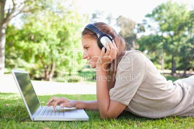 Side view of a woman with headphones and a laptop on the lawn