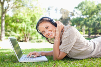 Side view of a smiling woman with headphones and a laptop lying