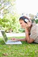 Side view of a woman with a laptop and headphones on the lawn