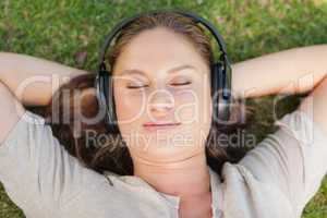 Relaxed woman lying on the lawn while listening to music
