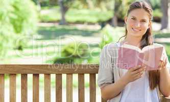 Smiling woman reading a book on a park bench