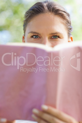 Woman hiding her face behind a book in the park