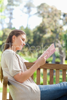 Side view of a woman reading a book on a park bench