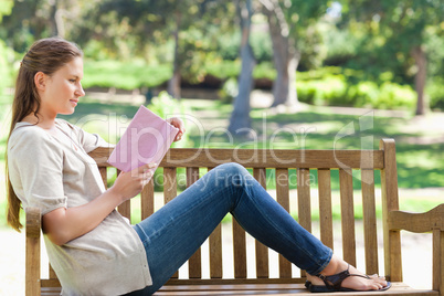 Side view of a woman reading a novel on a park bench