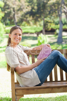 Side view of a smiling woman with a book on a park bench