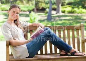 Side view of a smiling woman with her book sitting on a park ben