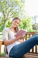 Smiling woman sitting on a bench in the park with a book