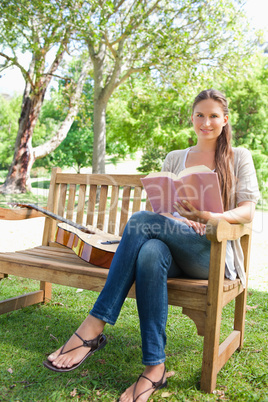 Smiling woman sitting on a bench with a guitar and a book