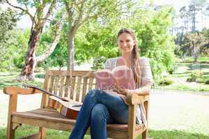 Smiling woman with a book and a guitar sitting on a bench