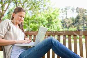 Side view of a smiling woman on a bench with her laptop