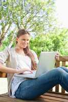 Smiling woman with her laptop sitting on a bench