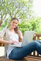 Smiling woman with a laptop sitting on a park bench