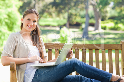 Smiling woman with her laptop on a park bench