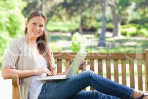 Smiling woman with her laptop on a park bench