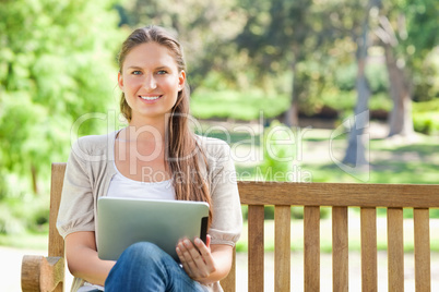 Smiling woman with a tablet computer on a park bench