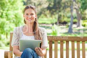 Smiling woman with a tablet computer on a park bench