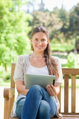 Smiling woman on a park bench with a tablet computer
