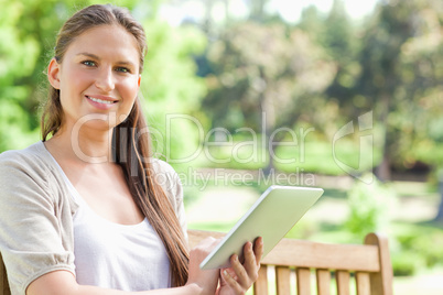 Smiling woman with a tablet on a park bench