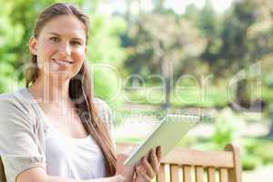 Smiling woman with a tablet on a park bench