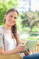 Smiling woman with her tablet on a park bench