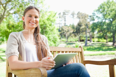 Smiling woman on a bench in the park with her tablet computer